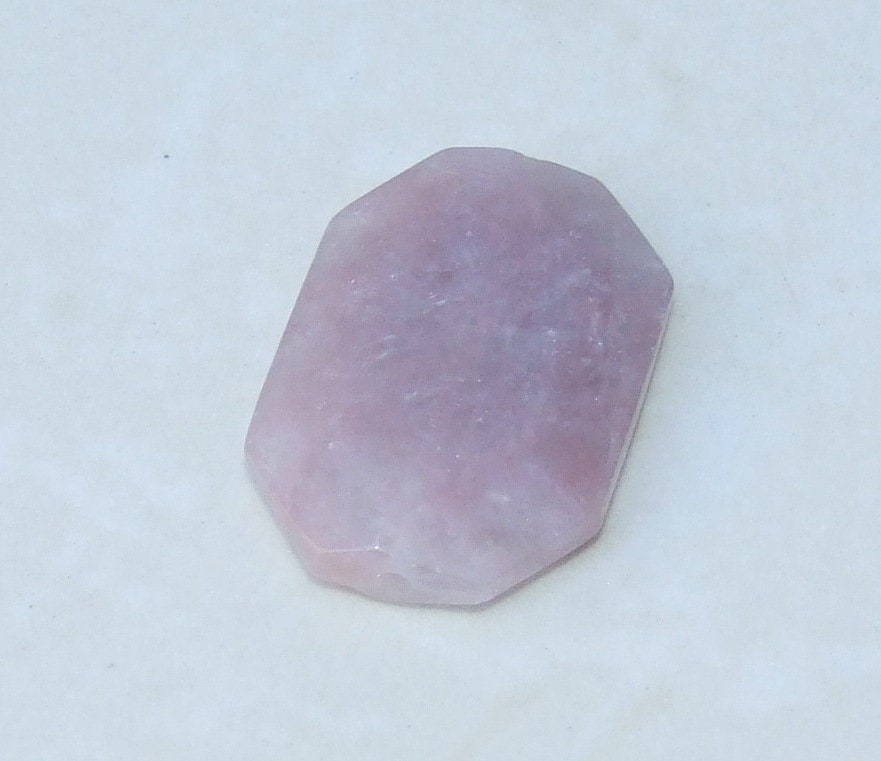 May include: A pale pink, faceted, gemstone with a smooth, polished surface.